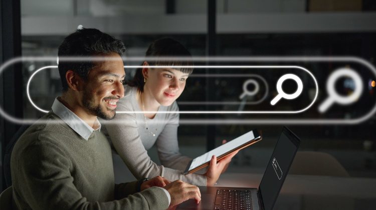 Dois profissionais sorrindo enquanto analisam informações em um laptop e tablet, com ícones de pesquisa sobrepostos na imagem.